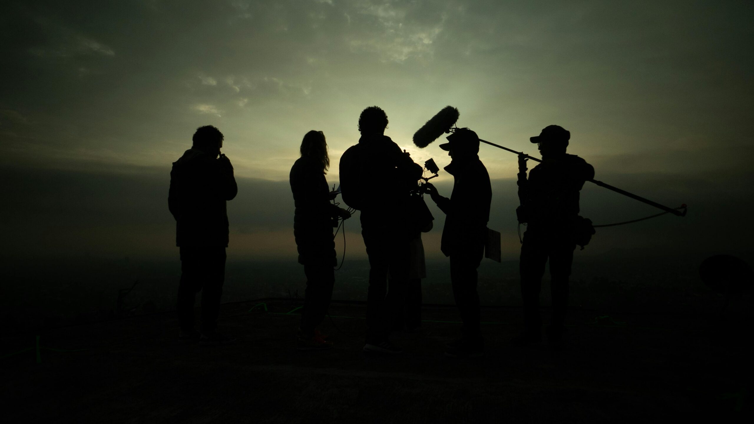 Film crew silhouettes against a dramatic sunset, capturing the art of movie making.